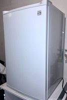 Front and side view of a white Kenmore bar fridge showing the outer door and Kenmore logo.