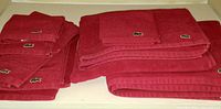 View of larger and smaller red towels stacked, each with Lacoste logo