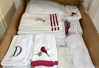 Large drawer filled with folded white hand towels, some embroidered with red cardinal birds and one with monogram 'D'.