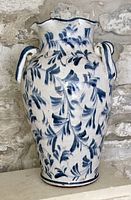 Front view of tall ceramic vase showing scalloped rim, handles and blue leaf motif