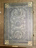 Front cover showing black leather with embossed floral and shell patterns and gold accents.