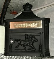 Front view of black cast iron mailbox showing detailed horse rider relief and brass plaque with LETTERS.