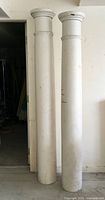 Full view of two tall white painted antique architectural columns side by side showing height difference and overall condition.