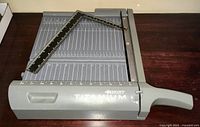 Photo showing the entire Westcott Titanium paper cutter on a dark wooden surface, including the cutting arm and measurement grid base.