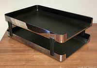 Two-tier in-out letter tray on wooden surface, showing black trays and chrome sides