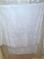 Full view of vintage white linen tablecloth showing embroidered floral corner and scalloped edges.