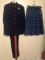 Full view of uniform jacket and pants side by side with blue and green tartan kilt hanging separately.