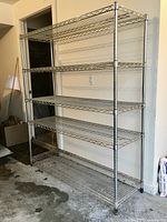 Full view of the shelving unit showing five tiers of chrome wire shelves against a wall in a garage or similar area.