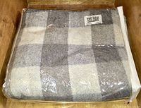 Top-down view of folded blanket in plastic packaging showing grey and off-white check pattern