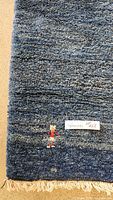 Close-up of the blue wool carpet showing texture, color shades, a small colorful motif, and fringed edge with a lot label.