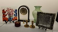 Front view of the lot showing glass plate with floral design, Grace Quartz clock, brass candlesticks and snuffer, silver faux finish plate, and green vase