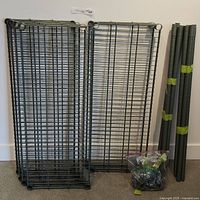 Wire grid shelves and tubular legs standing against a wall with a bag of plastic parts on the floor.