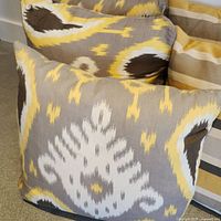 Photo showing square decorative pillows with a gray background and yellow, white Ikat pattern