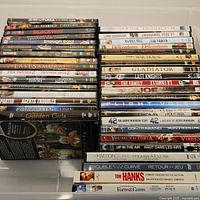Two stacks of DVDs showing the collection of 38 DVDs with visible titles including '3:10 to Yuma', 'The Rainmaker', 'Blackway', 'Enough Said', 'The Last Samurai', 'Gladiator', 'Golden Girls', 'Forrest Gump', and others.
