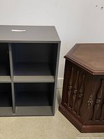 Grey cube cabinet with four compartments seen beside a hexagonal wooden side table.