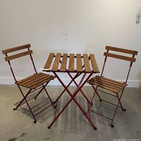 Full view of the red metal and wooden patio set with two chairs and a table shown against a light wall and floor.