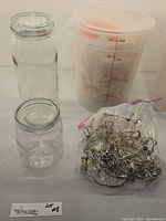 Two Ikea glass jars with glass lids, clear 8-quart measuring bucket with red measurement markings, and a bundle of metal clips in a bag.