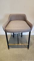 Grey upholstered chair with black metal legs and brass footrest seen from front