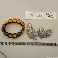 Close-up of amber-colored faceted stone stretch bracelet, three silver-tone filigree leaf brooches, and rhinestone tennis bracelet.