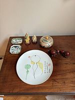 Overview of the entire 8-piece collection arranged on a wooden table showing all items including plates, figurines, jar, and carved item.