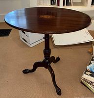 Front angled view of the oval wooden accent table showing the round wooden top, single pedestal with three curved legs ending in claw feet.