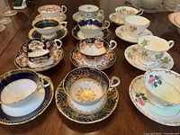Overview photo showing all 12 porcelain teacup and saucer sets arranged on a wooden surface, highlighting different patterns and colors.