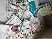 Assorted dish towels and cloths showing floral, striped, musical note and owl designs with a mix of colors including white, blue, green, purple, and beige.