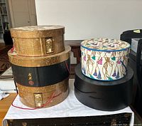 Four hat boxes in various designs and sizes displayed on a white cloth on floor