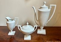 Photo showing the full set of three pieces: teapot, sugar bowl with lid, and creamer, all white porcelain with pedestal bases