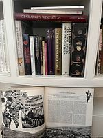 Image shows multiple hardcover wine reference books on a shelf, including 'Oz Clarke's Wine Atlas' at top, with books of varying spine designs and colors, some with decorative wine bottle labels on the cover.