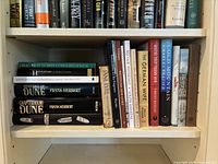 Bookshelf with fiction novels including Heretics of Dune and Chapterhouse Dune by Frank Herbert, Jane Eyre, The German Wife, Cold Mountain, Beloved.