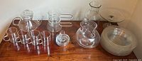 Photo of the glass teapot, cups, double boiler, pitcher, bowls, and cake stand arranged on a wooden surface.