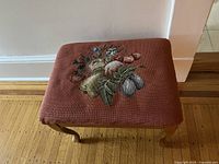 Top view of the ottoman showing needlepoint fruit design on maroon fabric.