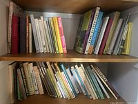 Books on wooden shelves showing a large variety of gardening and landscaping topics, with titles about trees, shrubs, herbs, garden design