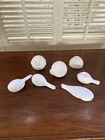 Top view showing all seven white plaster abstract sculptures arranged on wooden surface with window shutters background.