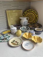 Photo showing the complete set of ceramic items arranged in a corner showing plates, bowls, pitcher and decorative containers with hand-painted floral and geometric designs.