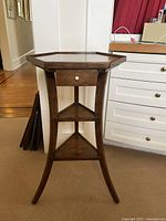 Full view of the hexagonal shaped wood side table showing front, drawer, shelves and legs.