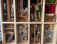 Top-down view of organized kitchen tool drawers showing various utensils including peelers, graters, scissors, and lobster crackers