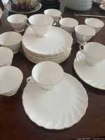 View of 12 white fine bone china teacups with matching plates with delicate gold trim, showing the elegant swirling pattern and classic design.