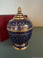 Blue and gold ceramic ginger jar on flat surface with original red box nearby.