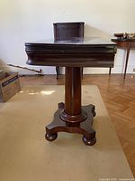 Side view showing folded table top, pedestal column and serpentine base with ball feet on casters.