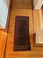 Top-down view of the Turkoman Chuval rug laid flat on a hardwood floor showing full geometric pattern and colors.