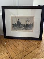 Black framed monochrome landscape print with white mat on wooden floor
