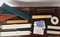 View of all slide rules, abacus, circular slide rule, carrying cases, and instruction booklets arranged on a dark surface.