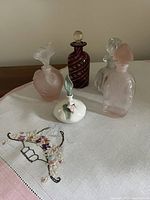 Five vintage perfume bottles arranged on a white surface, showing colors, sizes and stopper details. Included is a pink bottle with flower-shaped stopper with a chip.