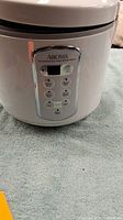 Front view of white Aroma electric rice cooker showing digital control panel with buttons and display screen.