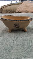 Side view of beige ceramic dish shaped like a small bathtub with floral design and blue trim on rim, resting on a grey towel.