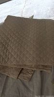 Folded beige quilted cotton coverlet in diamond pattern