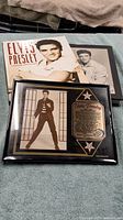Photo displaying Elvis Presley book with cover featuring his portrait and a framed plaque with a photo and biography.