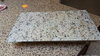 Top view of rectangular speckled granite-look stove top cover on a matching countertop, showing surface pattern and minor wear.